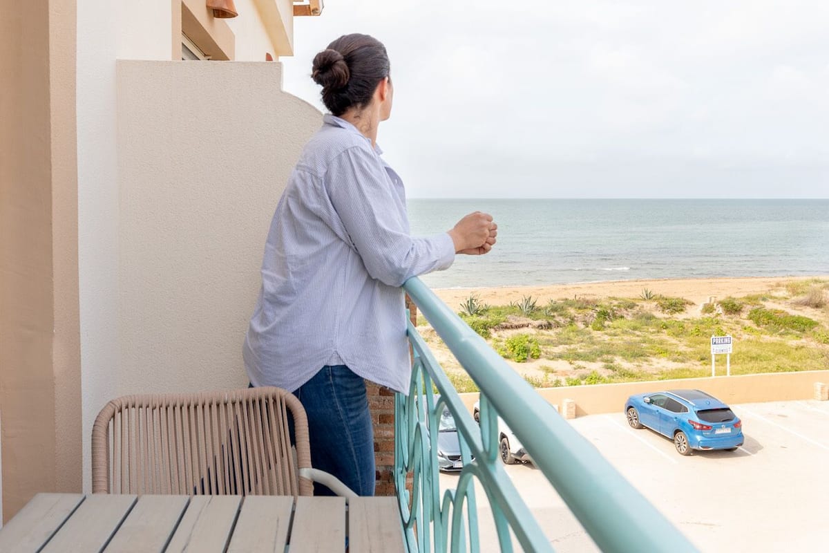 A person standing on a balcony overlooking a beach with a parking sign visible in the distance.