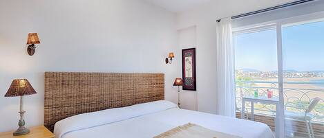 A bedroom with a large bed, a ceiling fan, and a view of the city through a balcony.