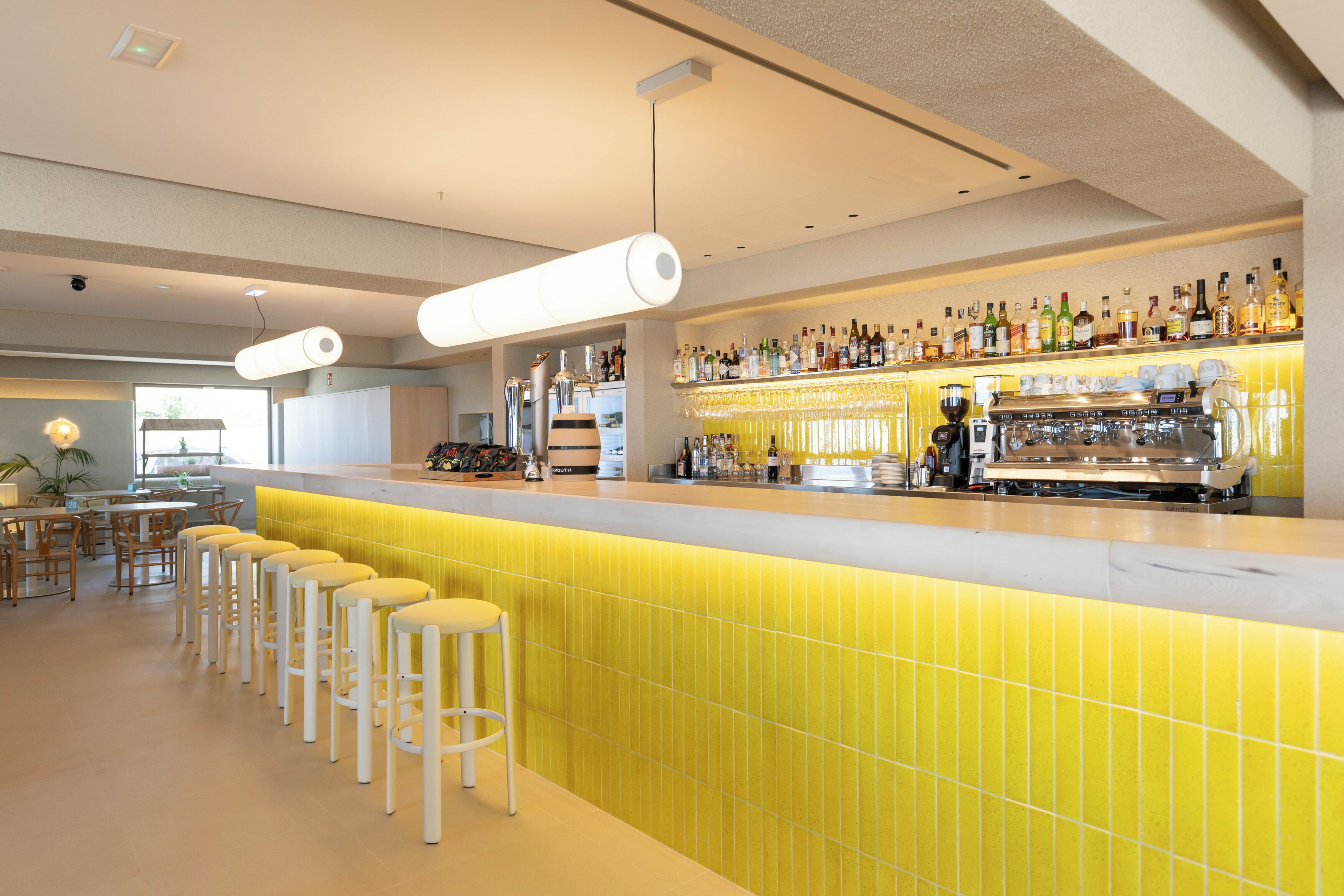 Zona de bar con taburetes, barra con botellas y máquina de café.