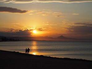 A sunset over a calm sea with silhouettes of two people on a beach. - Noguera Mar Hotel (Denia)