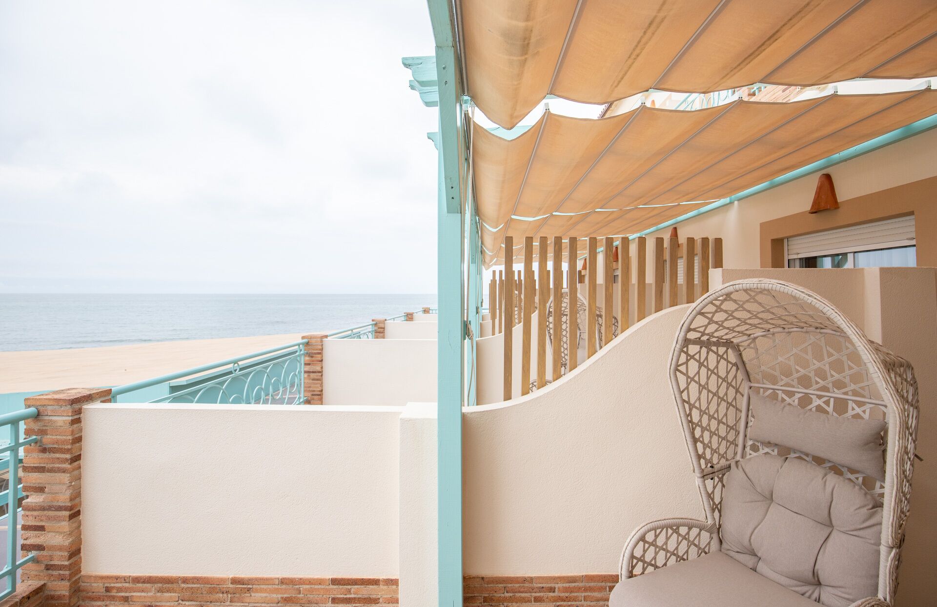 Ein Balkon am Strand mit einem Korbstuhl, Blick auf das Meer und einem Holzzaun.