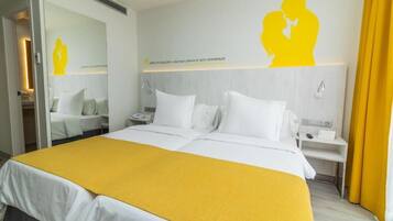 A hotel room with a large bed, a bedside table, a nightstand, and a mirror.