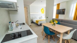 A compact hotel room with a kitchenette, a dining area with a table and chairs, a sofa, a TV mounted on the wall, and a bed with a yellow headboard. - Lemon & Soul Las Palmas (Las Palmas de Gran Canaria)