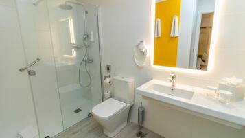 A modern bathroom with a glass-enclosed shower, a white toilet, and a sink with a mirror above it.