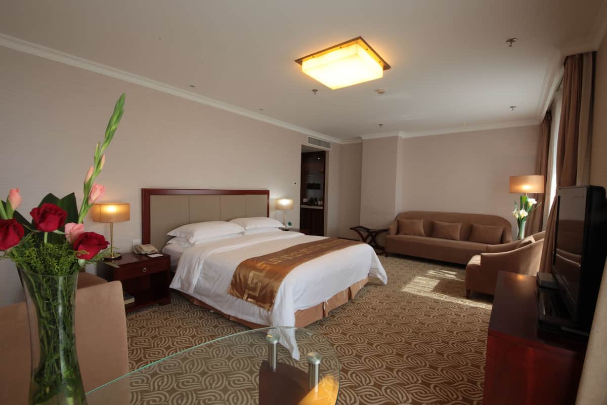 Habitación de hotel con una cama grande, un sofá, un televisor y un jarrón con flores.