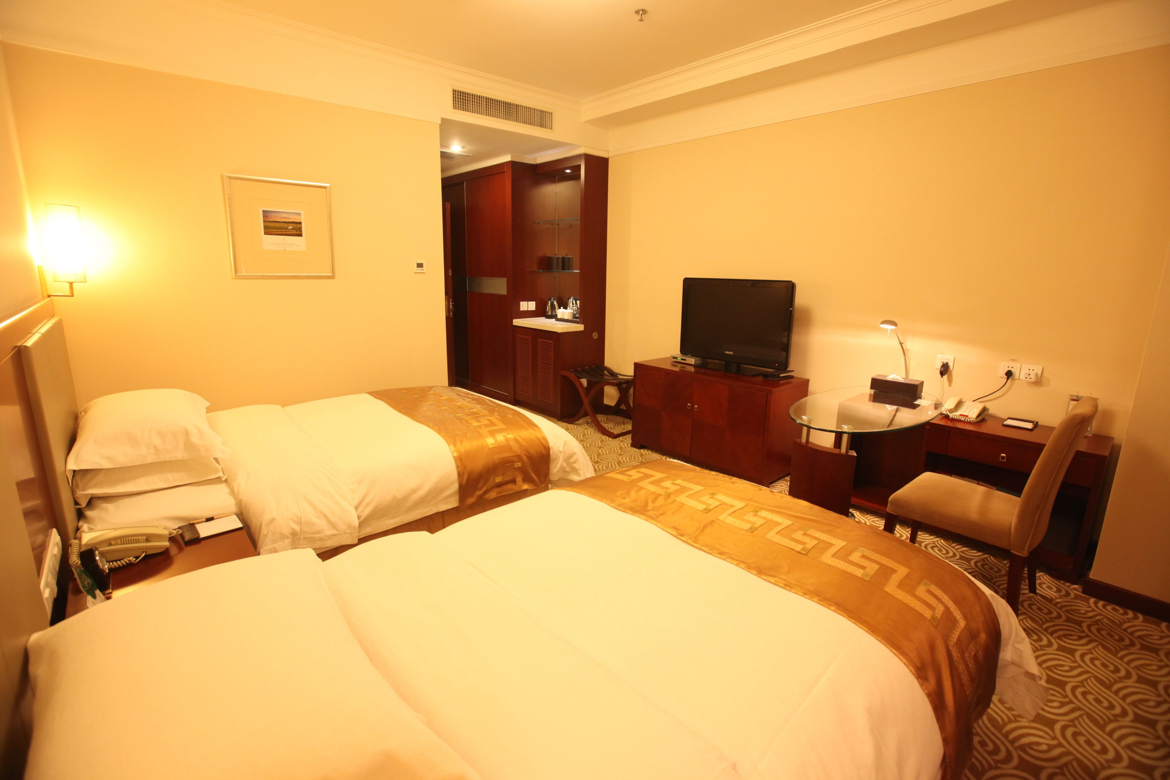 A hotel room with two beds, a desk, a television, and a bathroom visible through an open door.