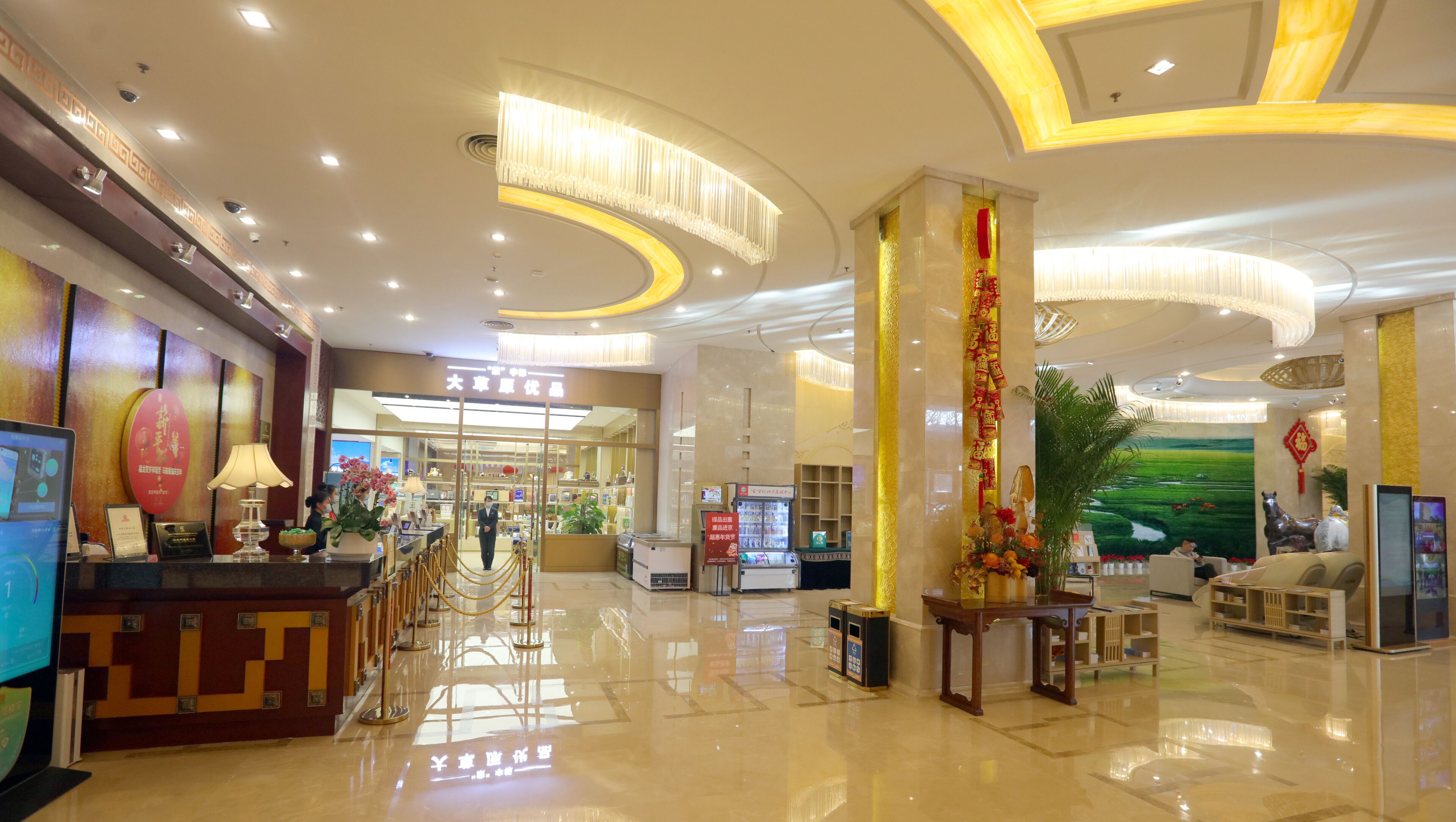 A hotel lobby with a reception desk, a digital screen, a large decorative column, and a seating area with a view of a green landscape.