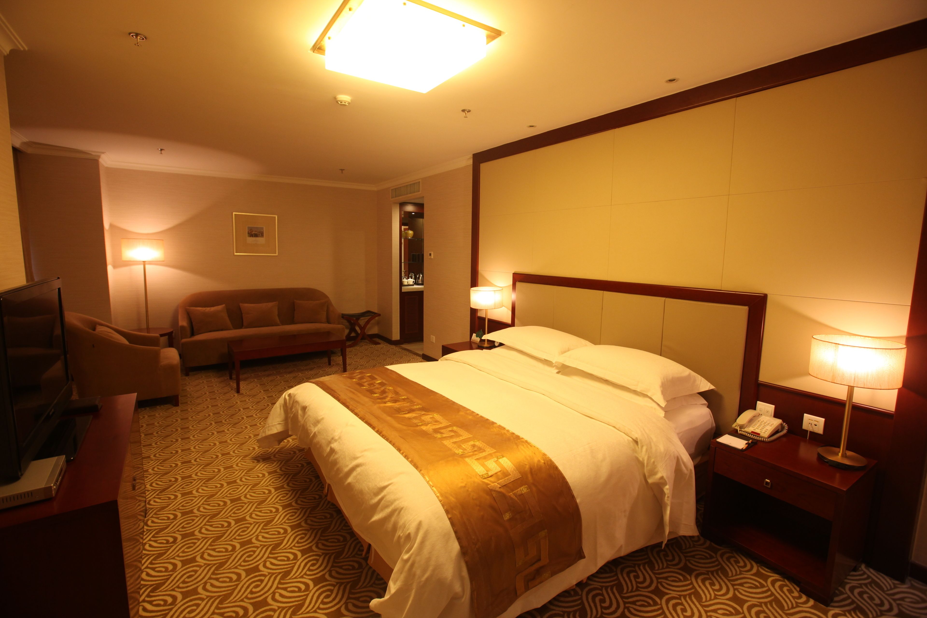 A hotel room with a large bed, a sofa, a desk with a lamp, and a television.