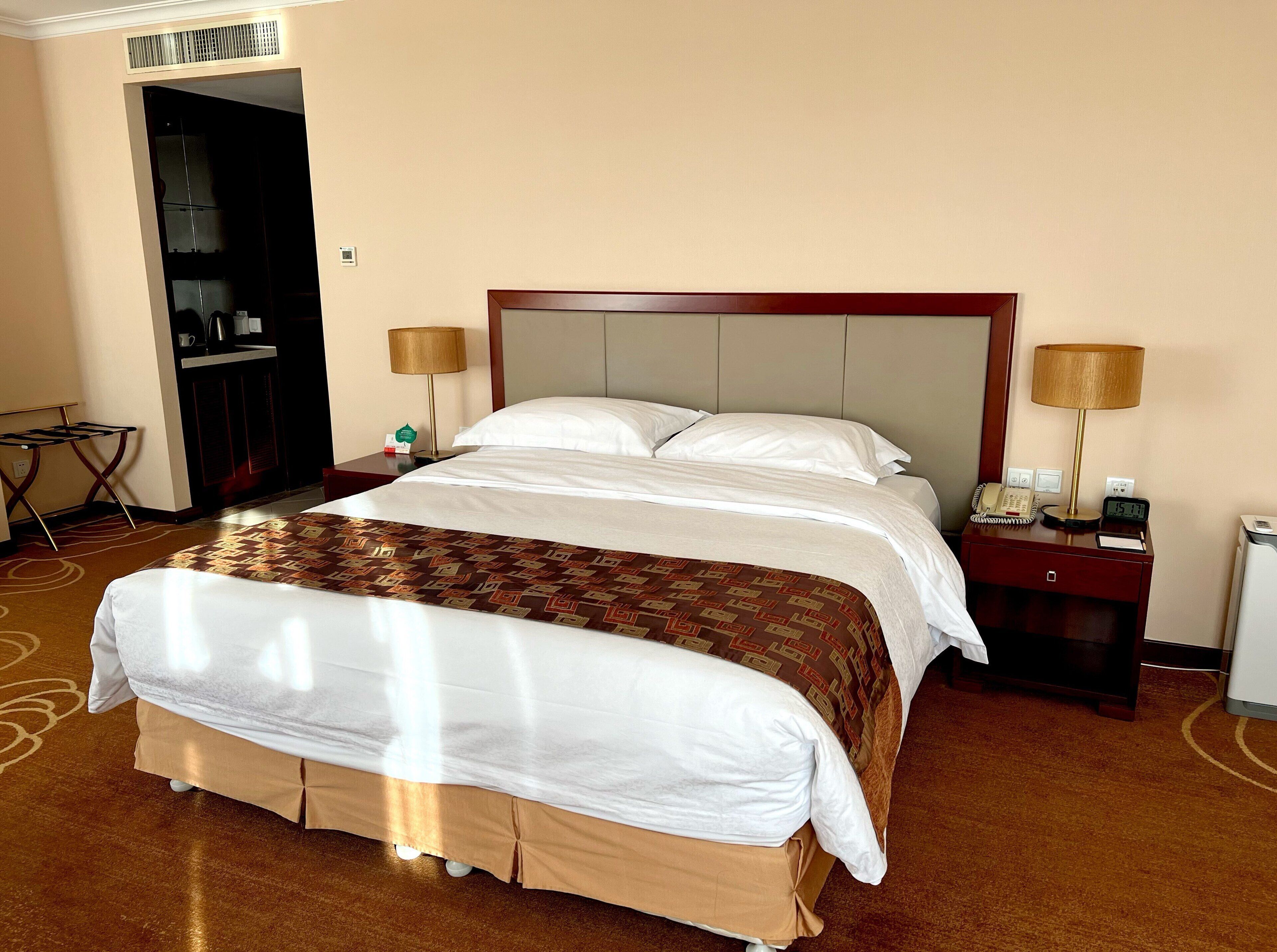 A hotel room with a large bed, two bedside tables, a desk, a chair, a wardrobe, and a mirror.