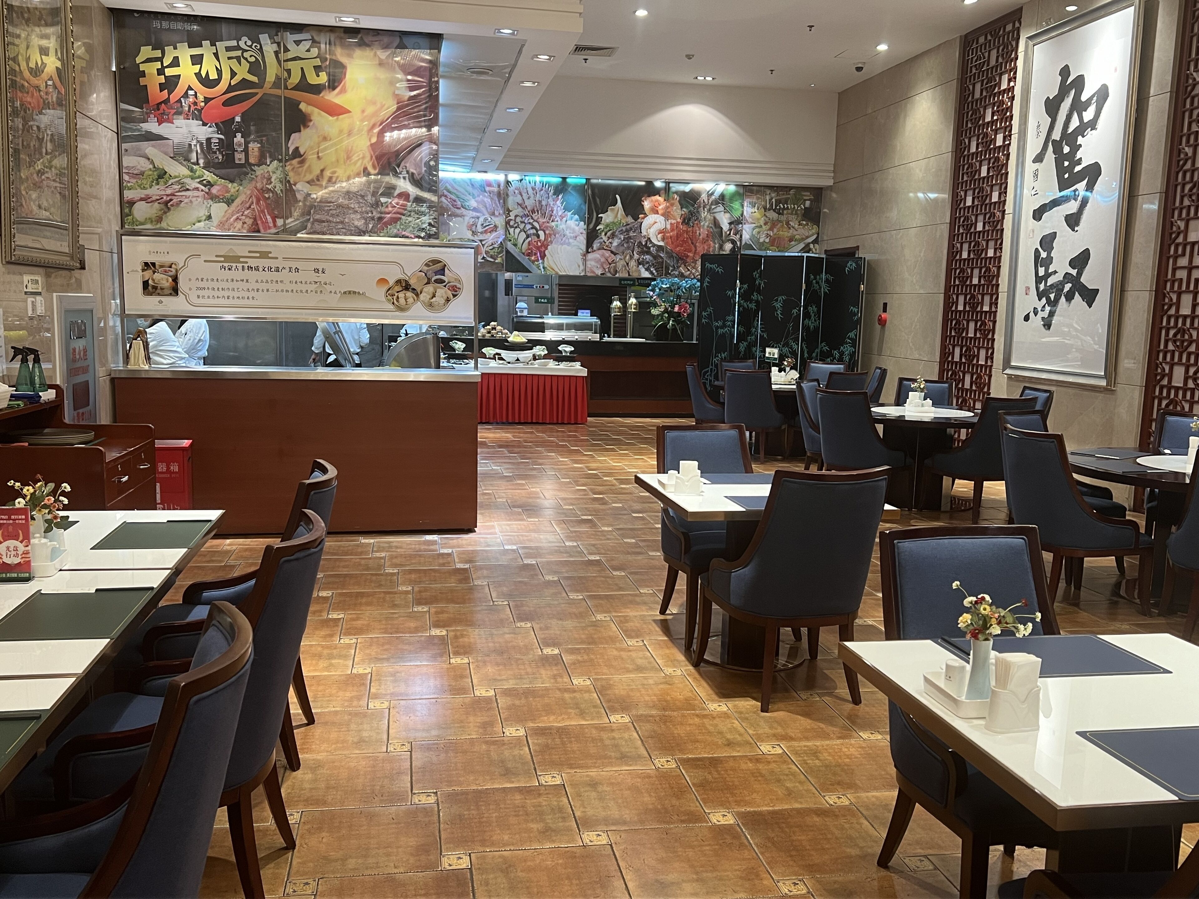 Interior de un restaurante con suelo de madera, mesas, sillas y una barra con mantel rojo.