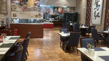 Interior de un restaurante con suelo de madera, mesas, sillas y una barra con mantel rojo.