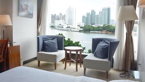 Hotelkamer met een bed, twee fauteuils, een tafeltje en uitzicht op een stadshemelbeeld en rivier.