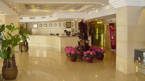 Een hotel lobby met een gebogen receptiebalie, potplanten en een decoratief model van een schip.