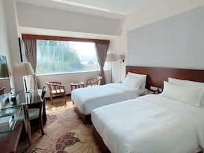 Une chambre d’hôtel avec deux lits, un bureau avec une chaise, une petite table et une fenêtre avec des rideaux.