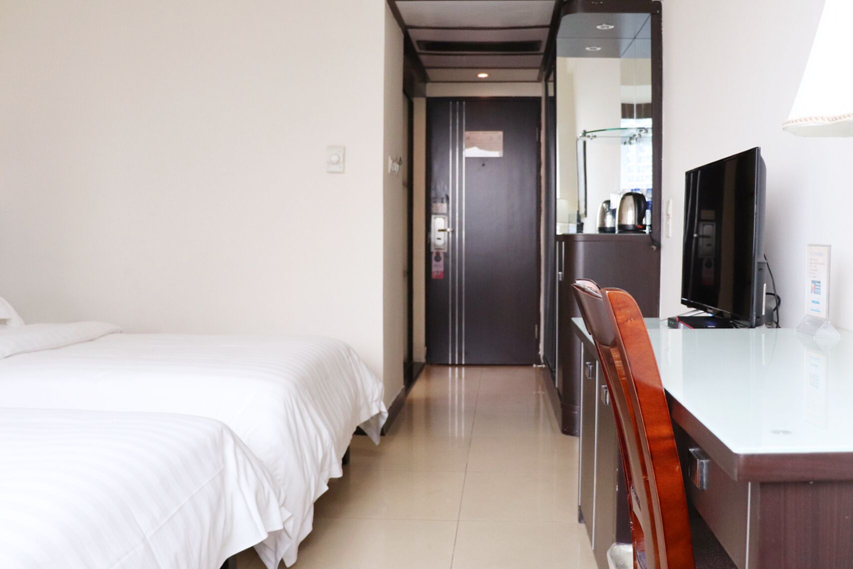 Habitación de hotel con una cama, un escritorio con silla, un televisor y un espejo.