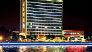 Een meerhoog hotel met verlichte reclameborden en een spiegeling in het water.