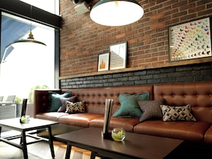 A modern interior with a leather sofa, a glass coffee table, and a brick wall with framed artwork. - Hotel Indigo Liverpool City Centre by IHG (Liverpool)