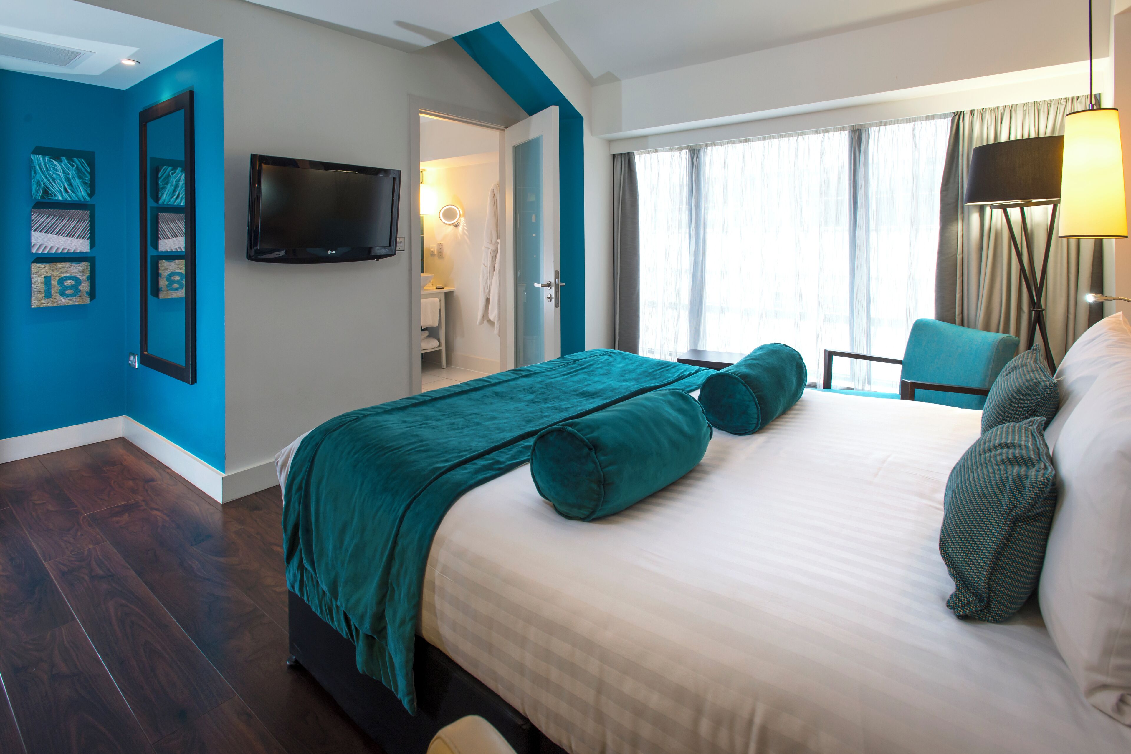 A modern hotel room with a large bed, a TV, a bathroom, and a view of the city.