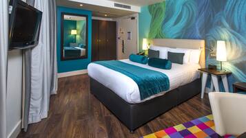 Une chambre d’hôtel avec un grand lit, une télévision, un miroir, une table de chevet et un tapis coloré.