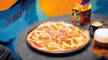 A pizza with various toppings, a box of fries, and a glass of beer on a table.