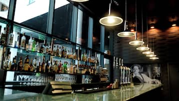 Een bar met meerdere flessenrekken en glazen, een toonbank en hangende pendelverlichting.
