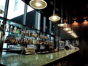 Un bar doté de plusieurs étagères remplies de bouteilles et de verres, d’un comptoir et de luminaires suspendus.