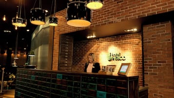 A reception desk with a brick wall background, a sign reading 'Hotel Indigo,' and a series of drawers below the desk.