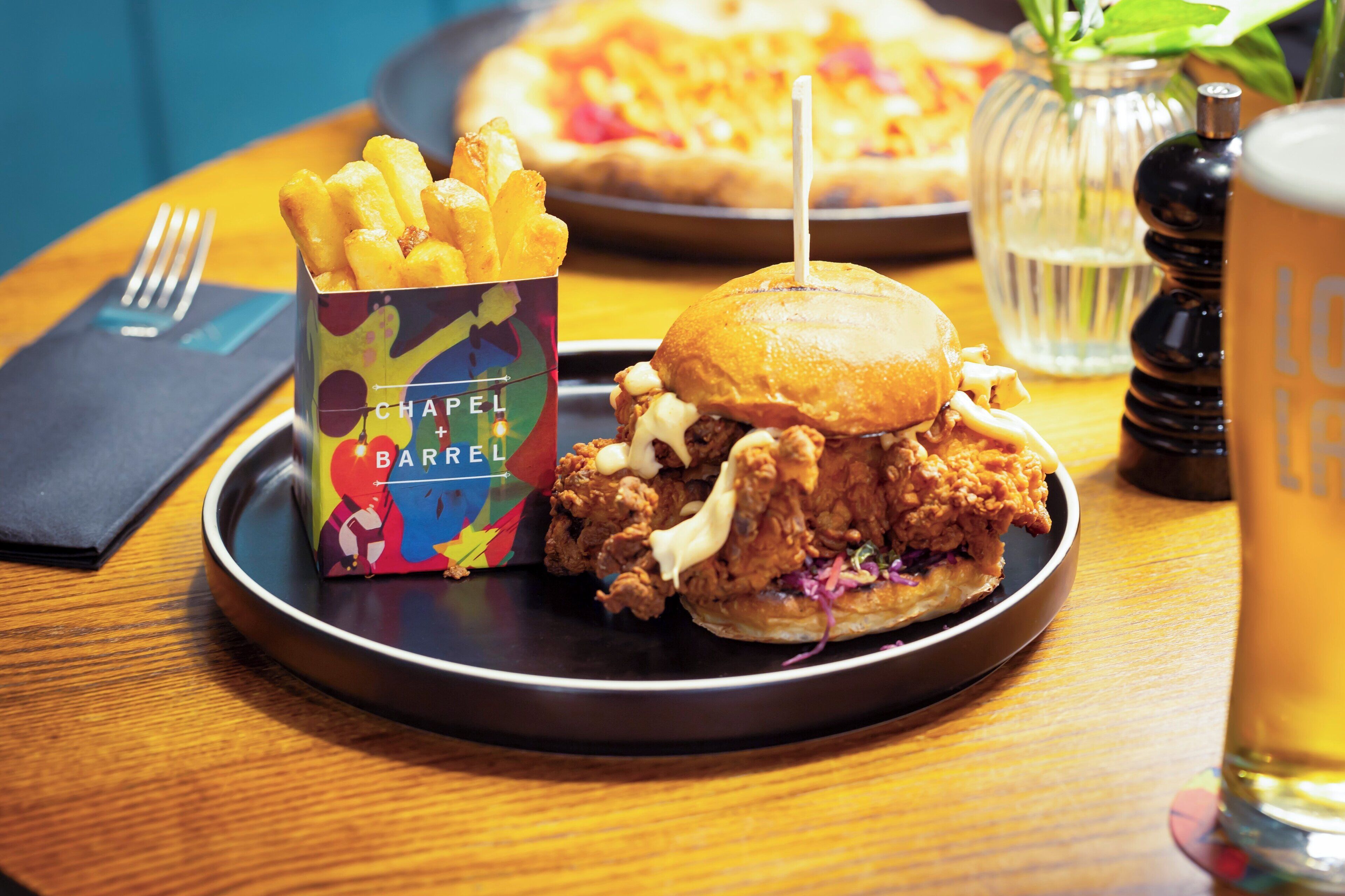 A meal with a chicken sandwich, fries, and a pizza on a wooden table.