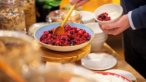 A buffet setup with a bowl of mixed berries and yogurt, a wooden serving board, and various food containers in the background.
