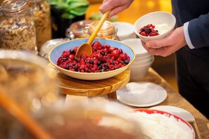 A buffet setup with a bowl of mixed berries and yogurt, a wooden serving board, and various food containers in the background.