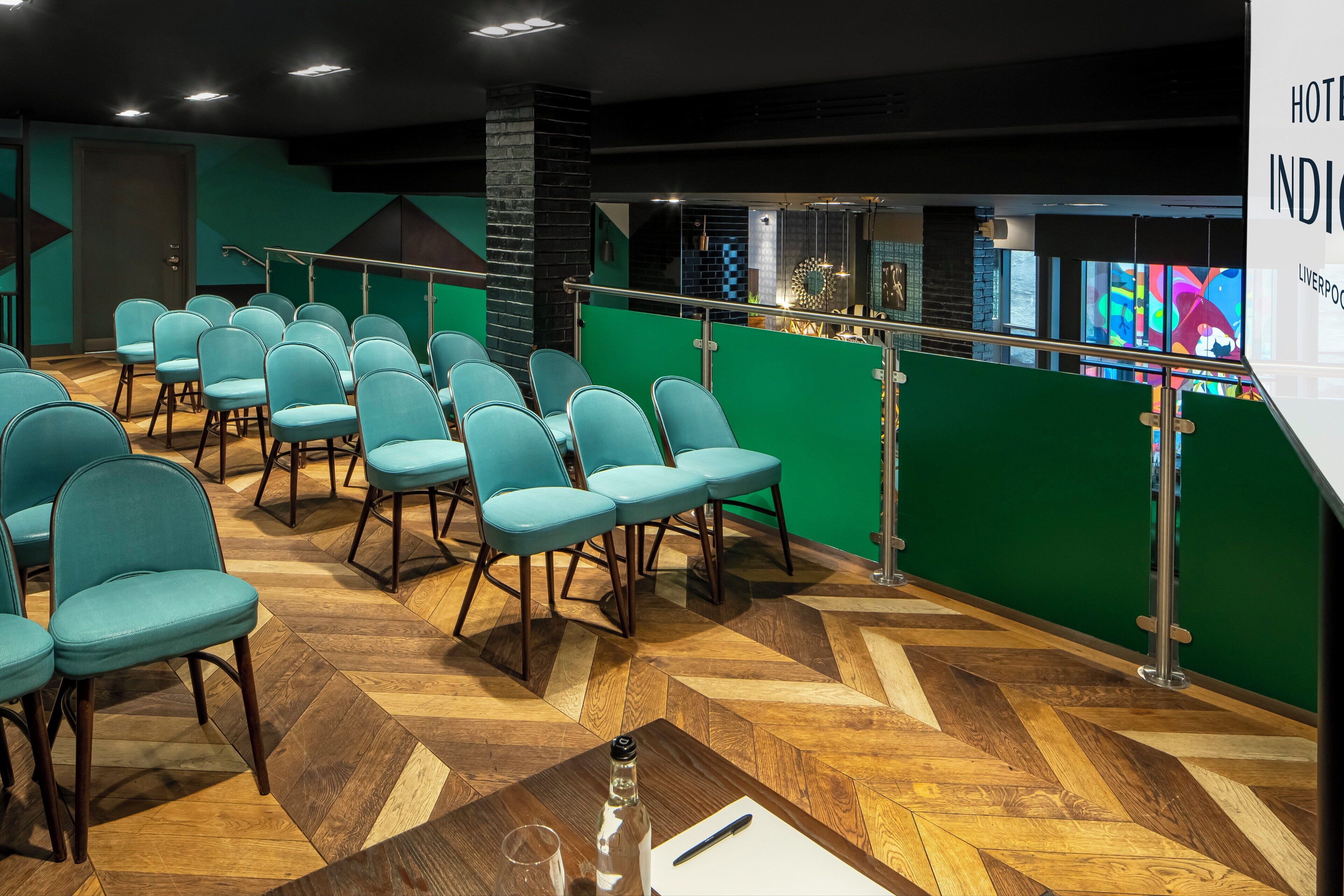 Un vestíbulo de hotel con filas de sillas color turquesa, piso con patrón de espiga y pared de acento verde.