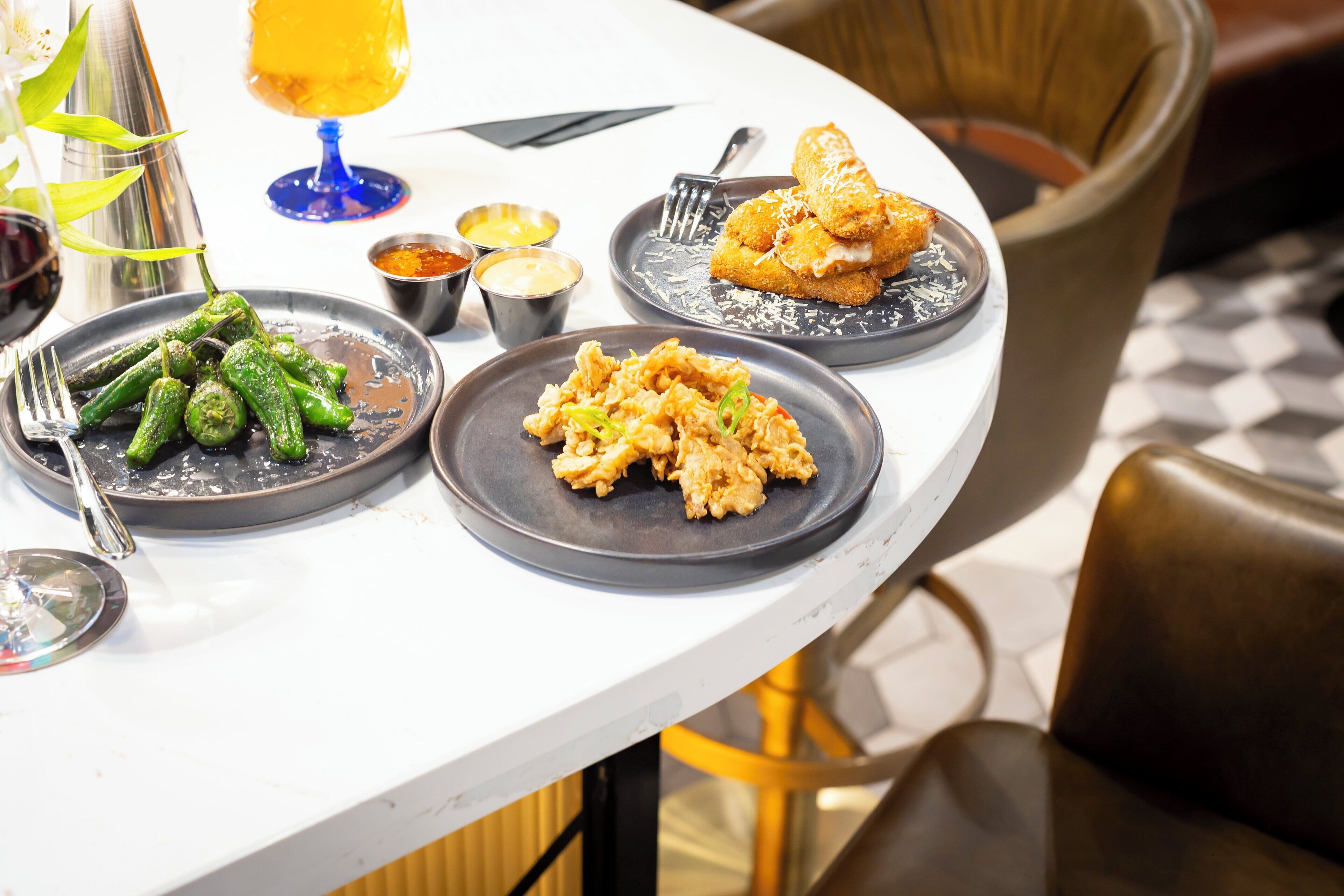 A dining table with plates of food, a glass of drink, and a cocktail shaker.