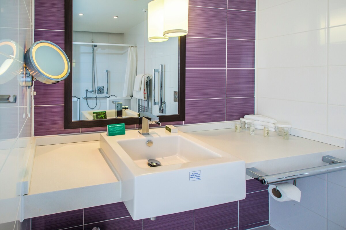 A modern bathroom with a large mirror, a sink, and a shower area.