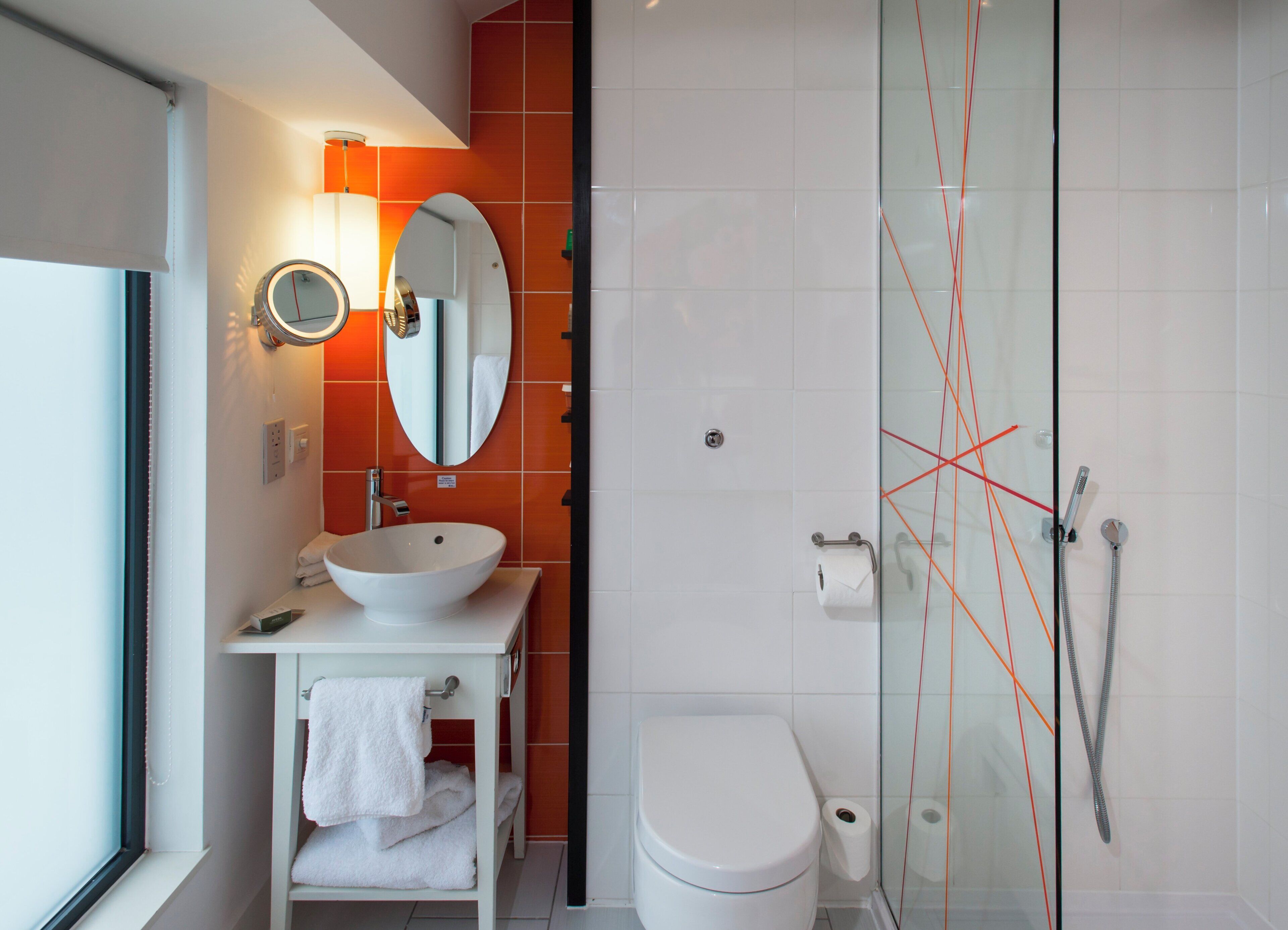 A modern bathroom with a white sink, mirror, and toilet, and a glass-enclosed shower area.
