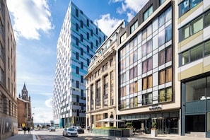 Un hôtel moderne à la façade classique, avec un bâtiment aux façades vitrées en arrière-plan, et un ciel bleu dégagé.