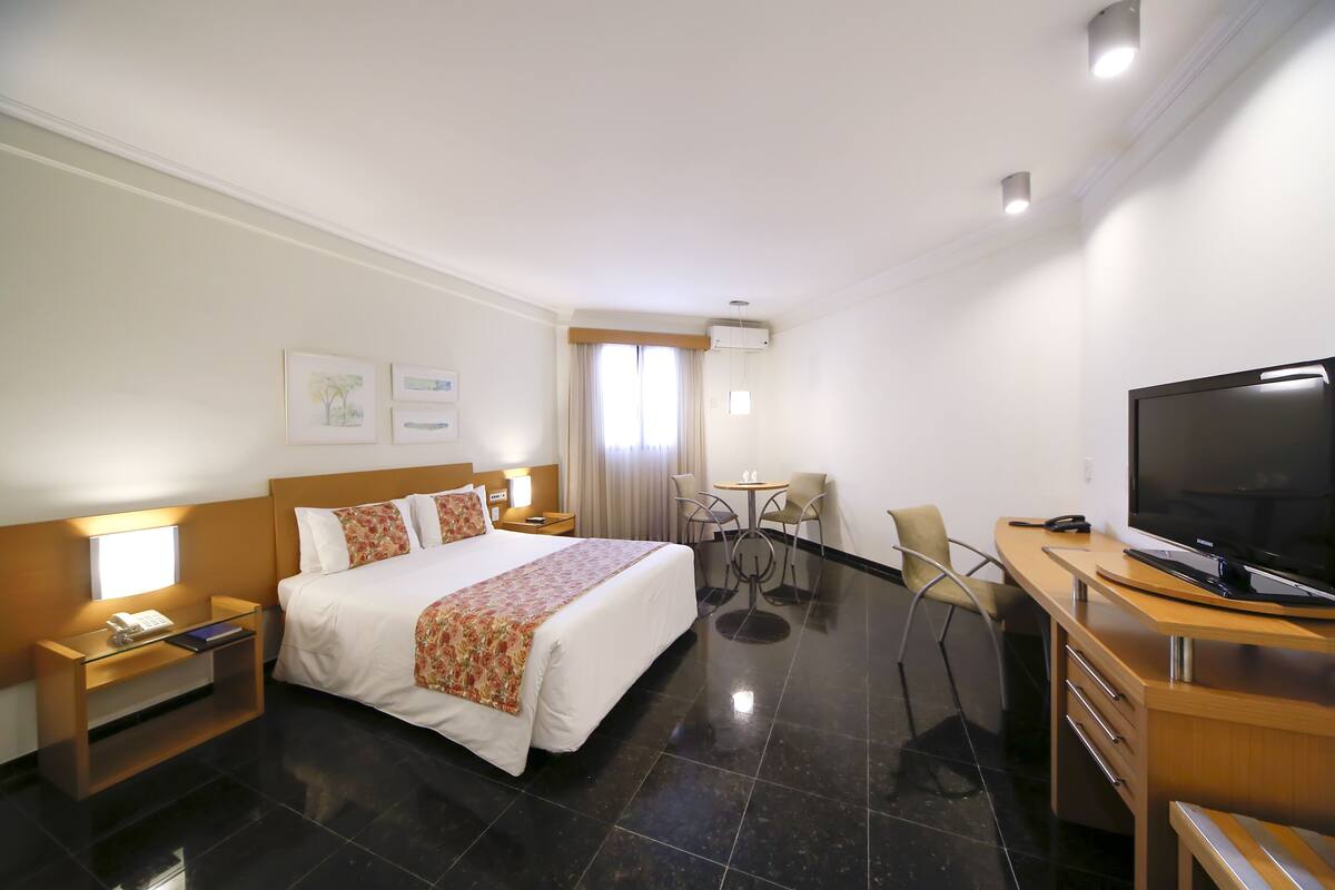 Une chambre d’hôtel avec un grand lit, des tables de chevet, un bureau avec une télévision et un petit coin repas.