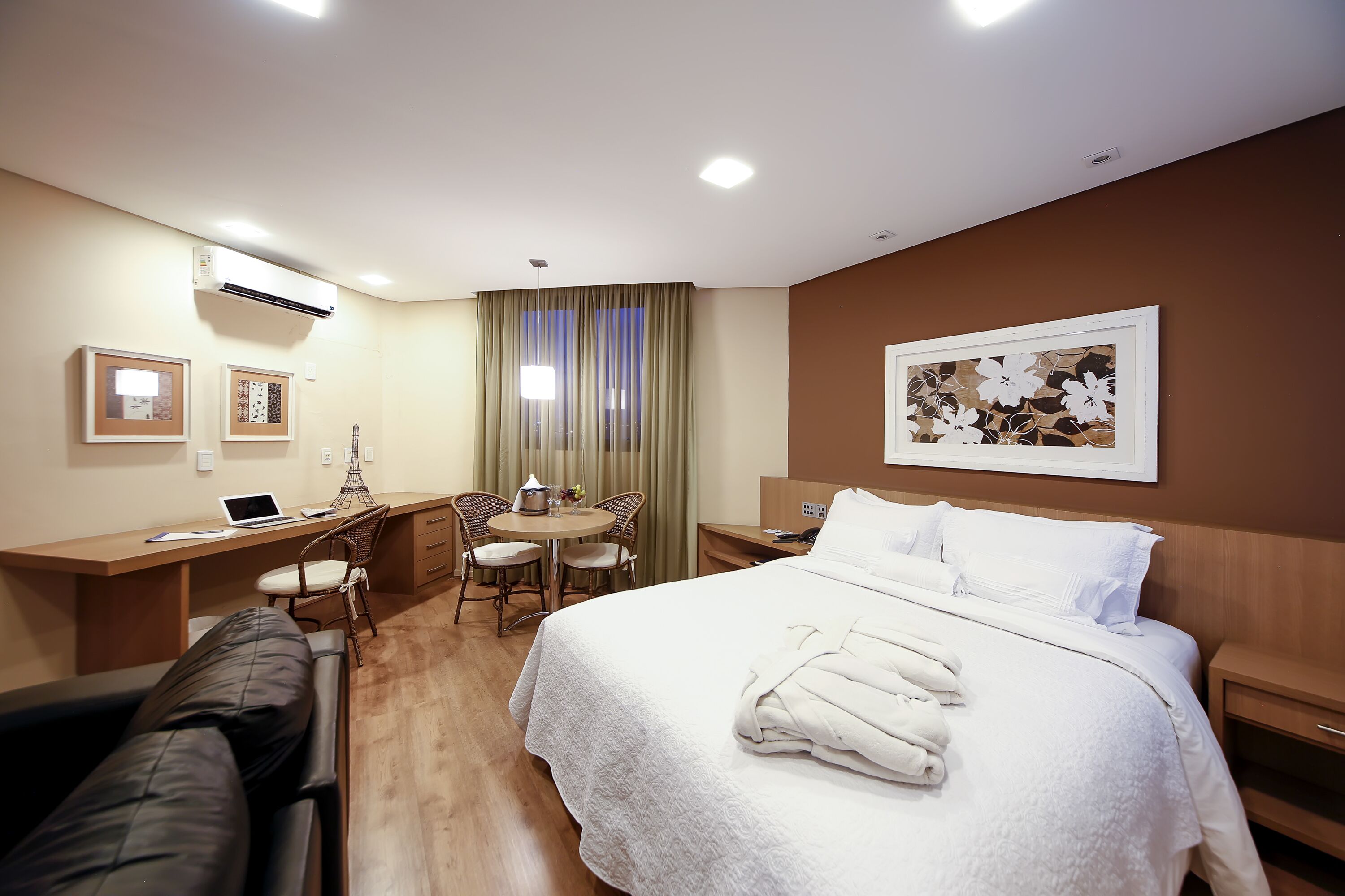 Quarto de hotel com cama, escrivaninha, cadeira e uma pequena mesa.