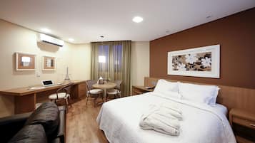 Quarto de hotel com cama, escrivaninha, cadeira e uma pequena mesa.