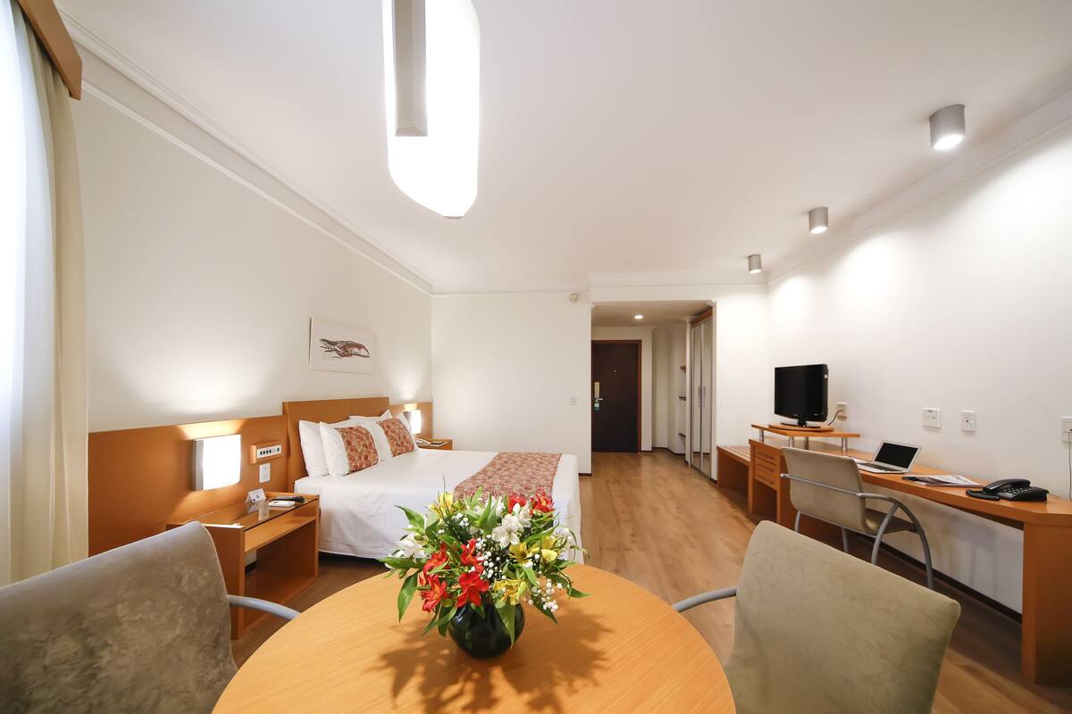 Une chambre d’hôtel équipée d’un lit, d’un bureau, d’une chaise et d’une table sur laquelle est posé un vase de fleurs.