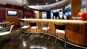 A bar area with a curved counter, several chairs, and a television mounted on the wall. - Grand Hotel Royal Sorocaba by Atlantica (Sorocaba)