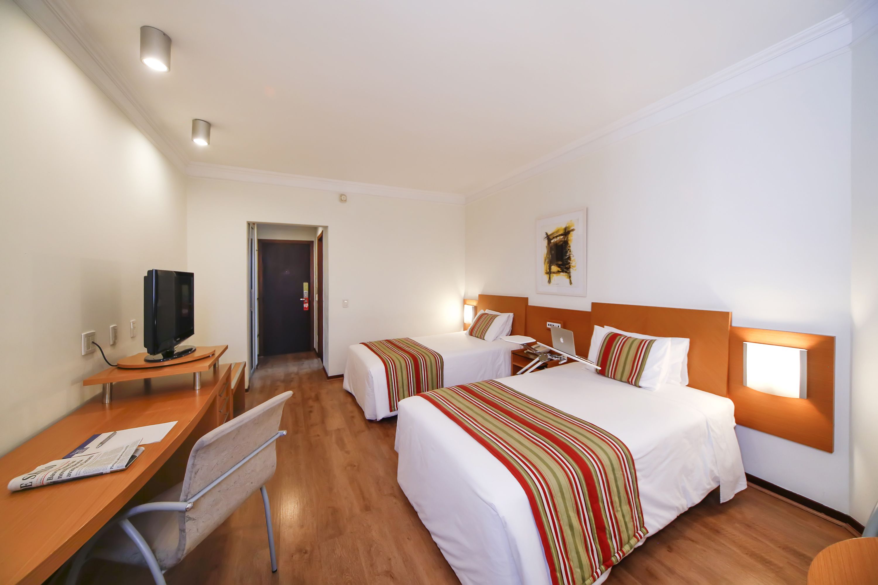 A hotel room with two beds, a desk with a computer, and a television.