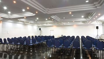 A conference room with rows of blue chairs, a polished black floor, and recessed ceiling lighting.