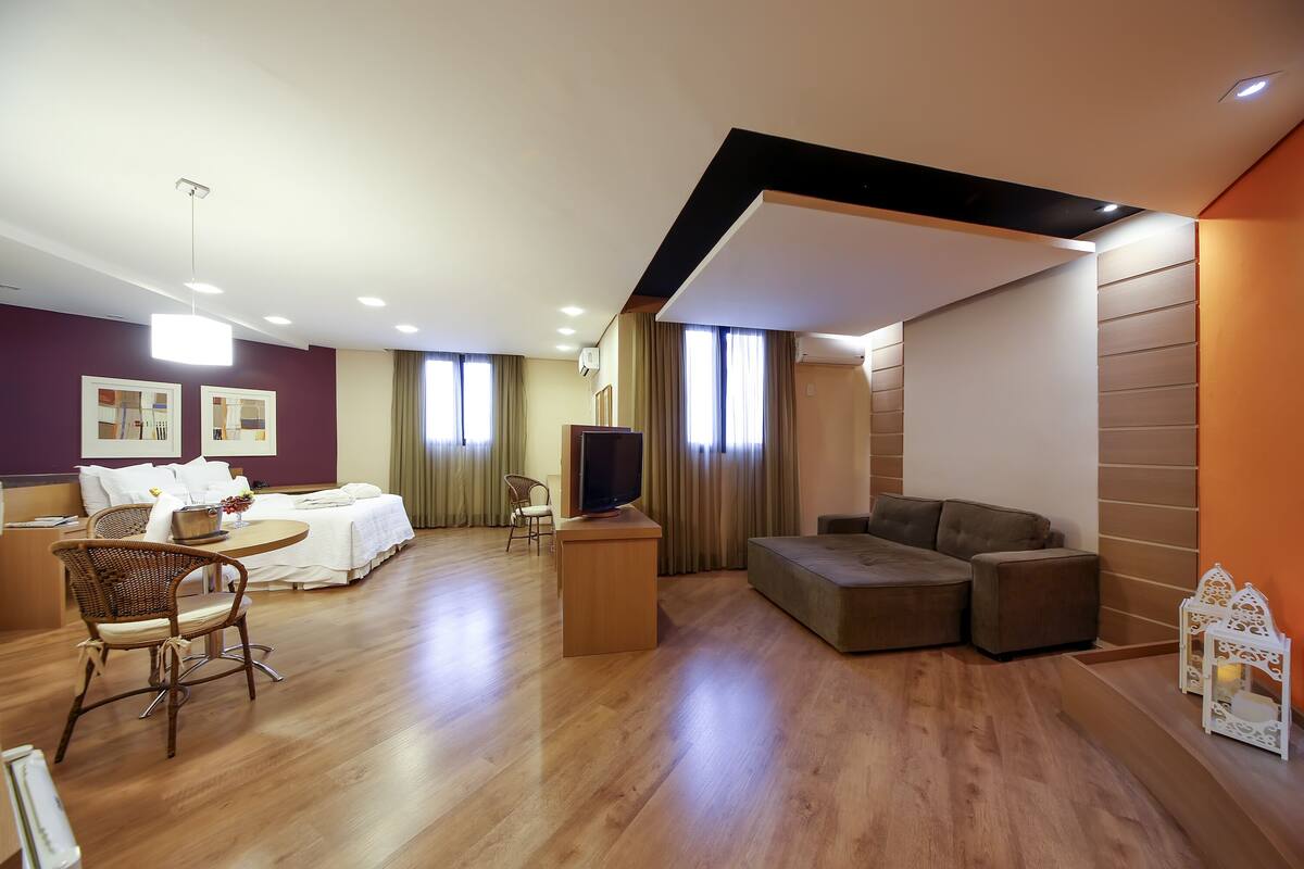 Une chambre d’hôtel moderne avec un plancher en bois, un coin repas comprenant une table et des chaises, un canapé, une télévision et une lanterne décorative.