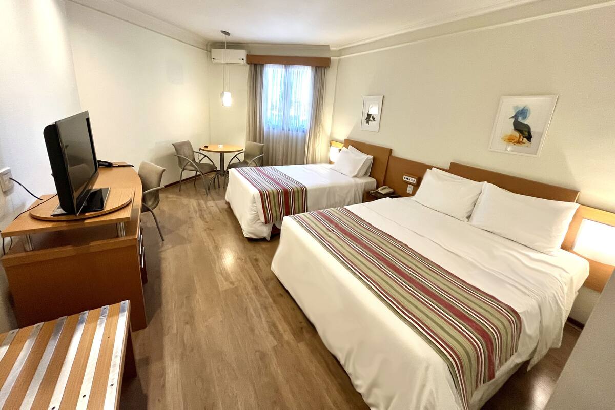 Une chambre d’hôtel avec deux lits, un bureau avec un ordinateur, une petite table et des chaises.