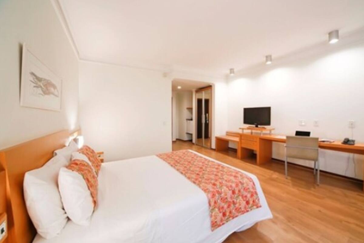 Une chambre d’hôtel comprenant un lit, un bureau, une chaise, un téléviseur et une porte donnant sur une autre pièce.