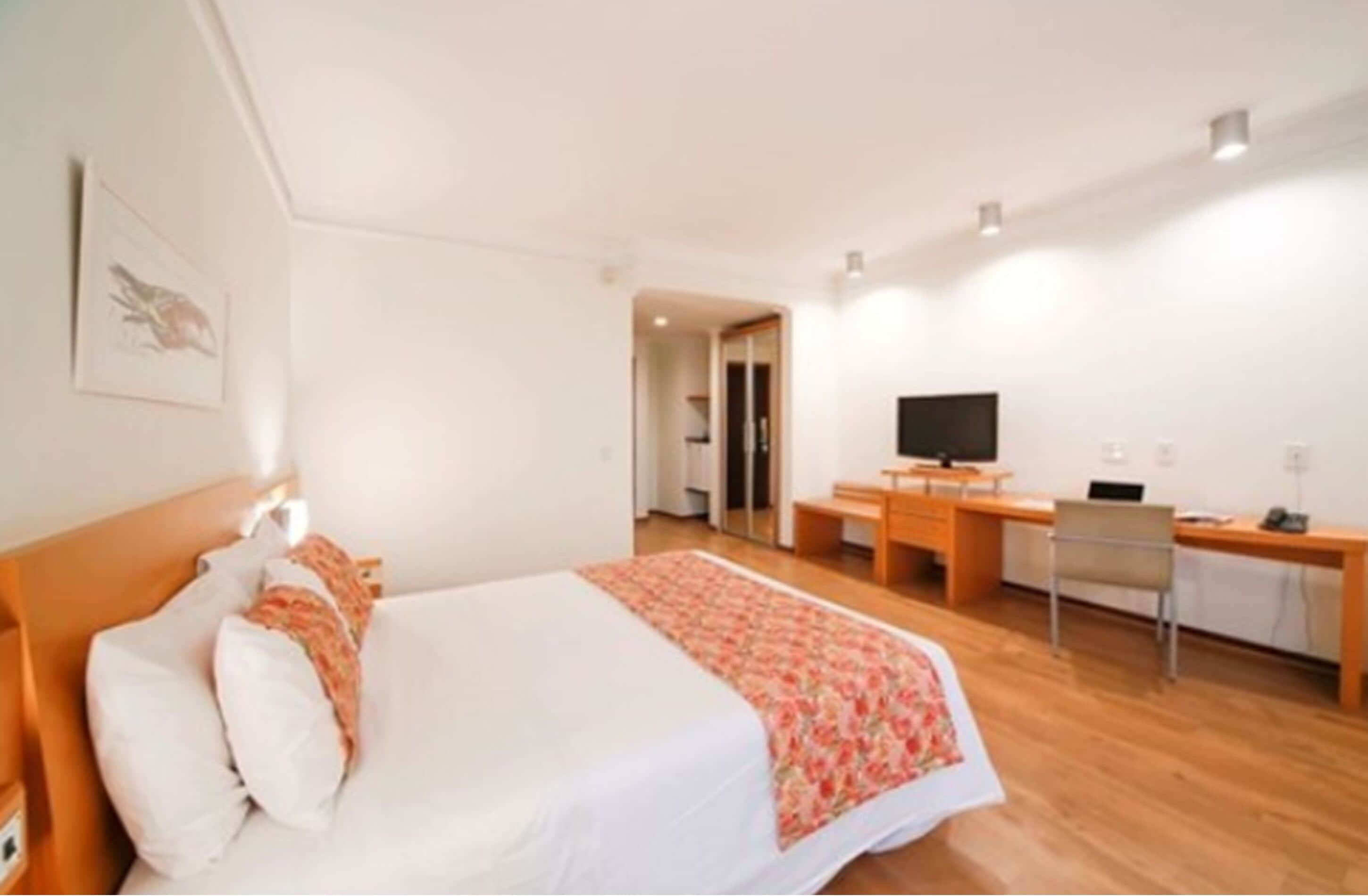 A hotel room with a bed, a desk, a chair, a television, and a door leading to another room.