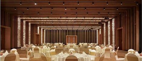 A banquet hall with round tables and white chairs, a patterned ceiling, and a carpeted floor.