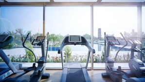 Un gimnasio con cintas de correr y equipo de ejercicio, ventanas amplias y vistas a palmeras y edificios.