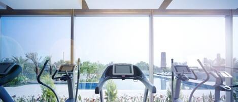 A gym with treadmills and exercise equipment, large windows, and a view of palm trees and buildings.