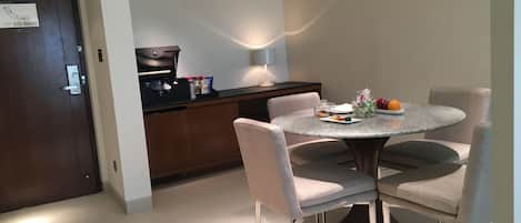 Un coin repas comprenant une table ronde, quatre chaises, une machine à café et une lampe.